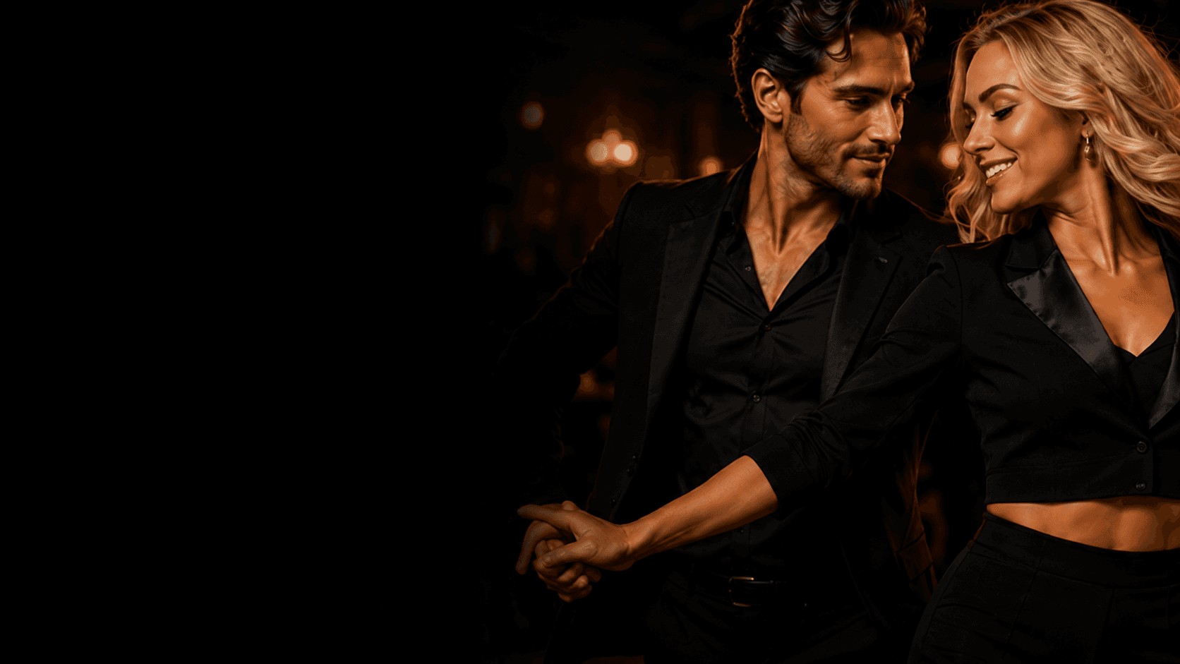 Elegant couple in black formal attire dancing together in a dimly lit, sophisticated ballroom.